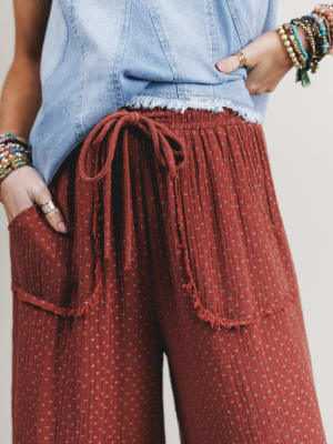 Close-up of waist and pocket detail of red patterned pants with a denim top and colorful bracelets.