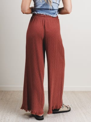Back view of woman wearing rust-colored wide-leg pants with a light background