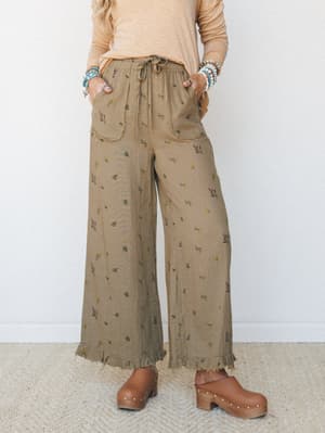 Wide-leg floral pants in a warm olive-khaki gauze fabric styled with a peach long-sleeve tee and wooden clogs — the kind of outfit that looks effortless but was absolutely thought about.
