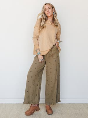 A relaxed, earthy outfit pairing wide-leg floral gauze pants with a sandy long-sleeve top and wood-soled clogs — the kind of put-together-without-trying look that makes people ask where you got your pants.