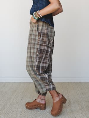 A side-profile shot of relaxed plaid pants in earthy olive and brown tones, styled with a denim corset top, stacked beaded bracelets, and tan studded clogs — the kind of outfit that looks effortless but was definitely thought about.