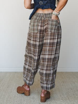 A back-view shot of relaxed wide-leg plaid pants in earthy brown and sage tones, styled with a cropped denim top and wooden clogs — the kind of outfit that feels effortless but definitely thought about.