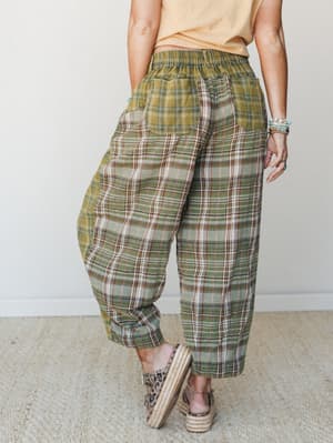 Shot from behind, a model wears roomy plaid wide-leg pants in earthy olive and cream tones paired with a soft peach crop tee and espadrille wedges — the kind of outfit that feels like a Saturday with nowhere to be.