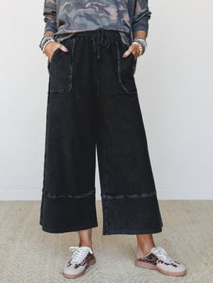 Wide-leg cropped denim-look pants in washed black styled with a camo sweatshirt and leopard sneakers — the kind of effortless combo that looks like you tried just enough.