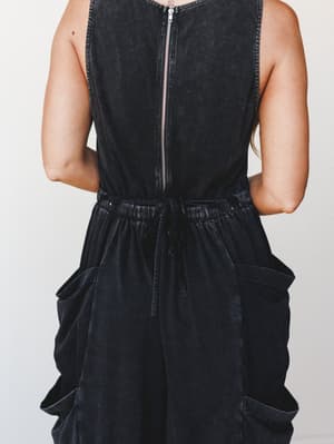 A close-up back view of a washed black cargo jumpsuit with a center back zipper, drawstring elastic waist, and oversized cargo pockets — relaxed and a little rugged in the best way.