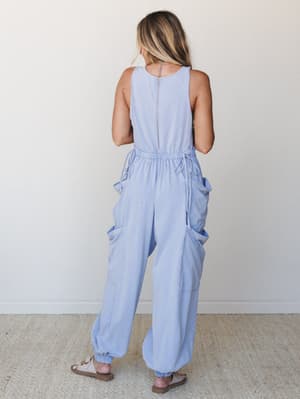 Shot from the back, this periwinkle cargo jumpsuit has a relaxed, lived-in feel — the elasticated waist with drawstring ties, oversized cargo pockets, and jogger-style ankles give it that effortless 'threw it on and it worked' energy.