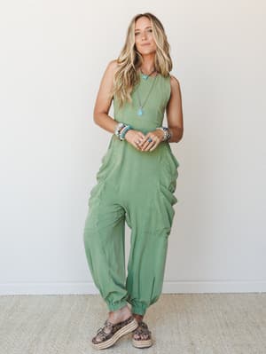 A relaxed, full-length sage green cargo jumpsuit styled with stacked beaded bracelets, a turquoise pendant necklace, and platform espadrille sandals — the kind of effortless one-and-done outfit that feels intentional without trying too hard.