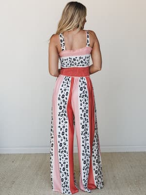 A wide-leg leopard print jumpsuit shot from the back, mixing coral, blush pink, and white in bold vertical color-block panels with a smocked bodice — the kind of piece that makes you feel like you packed the right thing.
