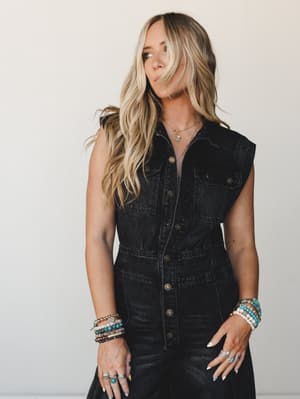 A black washed denim sleeveless jumpsuit styled with layered beaded bracelets, stacked rings, and a delicate gold necklace — the kind of outfit that looks effortless but definitely took a minute to put together.