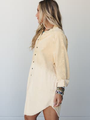 A corduroy tunic dress in a soft mustard-to-cream dip dye wash, styled with stacked beaded bracelets and a turquoise necklace — the kind of effortless, lived-in piece that looks just as good on a coffee run as it does anywhere else.