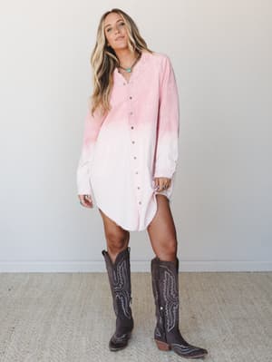 A relaxed, sun-kissed look — an oversized dip-dye corduroy tunic dress in blush-to-cream fading paired with tall dark brown cowboy boots and a turquoise necklace, shot against a soft neutral studio wall.