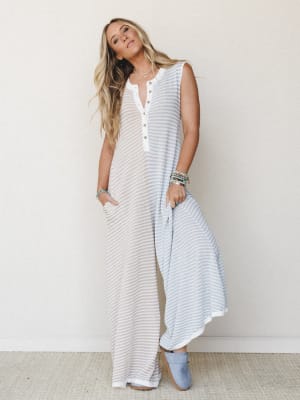 A relaxed wide-leg jumpsuit in a soft beige and blue stripe with a henley neckline — the kind of effortless piece that looks like you tried just the right amount, styled with stacked beaded bracelets and suede booties.