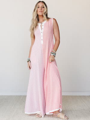A breezy striped maxi-length wide-leg jumpsuit in coral and white, styled with stacked beaded bracelets and flat woven sandals — the kind of effortless outfit that works just as hard at brunch as it does at the beach.