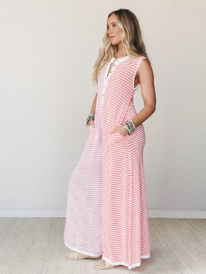 A breezy striped maxi jumpsuit in coral and white worn with stacked beaded bracelets and flat sandals — the kind of effortless one-and-done outfit that looks like you tried just enough.