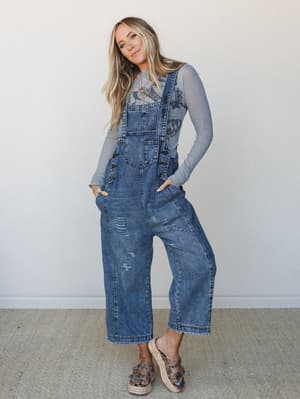 Wide-leg denim overalls styled over a long-sleeve gray layering tee, worn with platform espadrille sandals and layered necklaces — the kind of put-together-without-trying look that feels equally at home at the farmers market or a casual weekend brunc