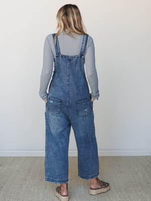 Shot from behind, a model wears acid-washed wide-leg denim overalls over a long-sleeve ribbed grey top, styled with leopard print espadrille platforms — the kind of laid-back, put-together look that makes errands feel intentional.