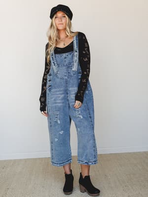 Acid-washed denim overalls styled with a black crochet long-sleeve top, baker boy hat, and black ankle booties — the kind of outfit that feels effortless but clearly had a thought behind it.