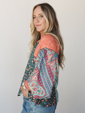 A mixed-print boho blouse in rich teal and coral paisley panels styled with denim, shot in soft studio light — the kind of top that does all the talking so you don't have to.