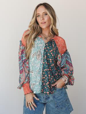 A mixed-print patchwork blouse in teal, sage, and coral paired with wide-leg denim — the kind of top that looks like it has a whole personality before you even put it on.