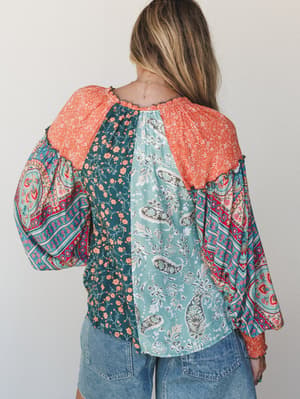 Shot from behind, a mixed-print blouse with balloon sleeves steals the show — patchworked in teal florals, soft paisley, and coral, paired with relaxed denim for an effortlessly expressive everyday look.