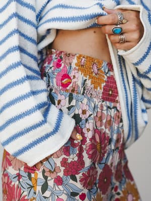 A close-up detail shot of a floral wide-leg pant styled with a blue striped textured sweater, stacked silver and turquoise rings adding that perfect lived-in boho finishing touch.