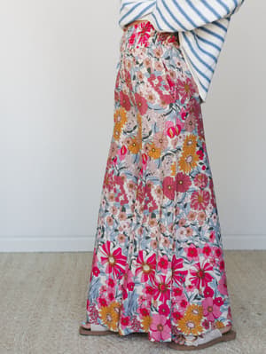 A bold retro-floral wide-leg pant in hot pink, marigold, and cream styled with a striped sweater — the kind of outfit that makes a Tuesday feel like a farmers market trip you actually planned for.