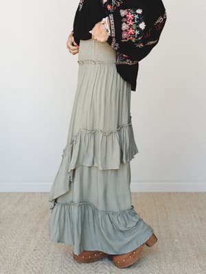 A tiered ruffle maxi skirt in dusty sage pairs with a black embroidered kimono top and wooden clogs — the kind of outfit that looks effortless but was absolutely thought about.