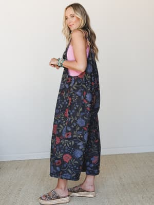 A model shot in three-quarter profile wearing wide-leg floral denim overalls over a pink tank, styled with stacked turquoise bracelets and leopard print platform sandals — the kind of outfit that looks effortless but absolutely isn't an accident.