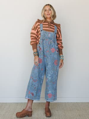 A floral-printed denim overall layered over a brown and coral stripe sweater — the kind of outfit that looks like it happened naturally but definitely did not.