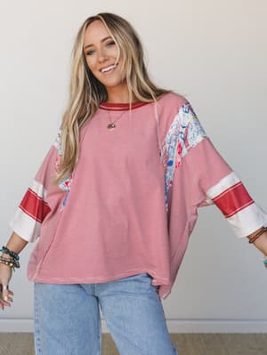 An oversized mixed-print top in red and white pinstripe with floral patchwork panels at the shoulders and sleeves, styled with light wash wide-leg jeans and layered bracelets — relaxed, cheerful, and very much a 'Saturday with nowhere to be' kind of