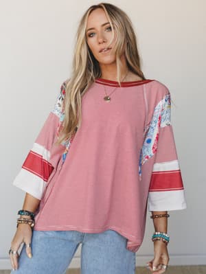 A relaxed mixed-print top in red and white pinstripe with floral patchwork sleeves and color-block bell cuffs, styled with light-wash jeans and layers of boho bracelets — the kind of top that looks like it came together effortlessly but definitely di