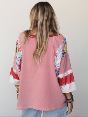 A back view of an oversized patchwork top in red and white pinstripe with mixed-print patchwork panels at the shoulders and fluted sleeves with contrast banding — worn with light denim and layered bracelets for an easy, lived-in boho feel.