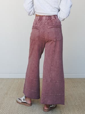 A back-view shot of wide-leg pants in a washed plum tone, styled with a cropped grey sweatshirt and leopard-print sandals — the kind of outfit that looks effortless but clearly had a moment of intention behind it.