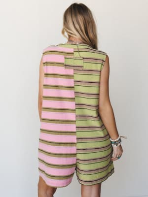 A back-view shot of a sleeveless mini dress in a playful color-blocked stripe design — pink on one side, lime green on the other — styled with stacked beaded bracelets and a delicate chain necklace for that effortless, collected summer feel.