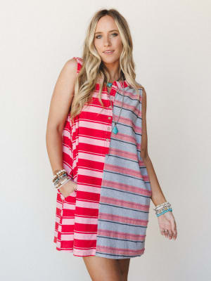 A colorblock striped mini dress split between bold red-and-pink stripes and softer grey-and-pink stripes, styled with stacked boho bracelets and a turquoise pendant necklace — easy, expressive, and made for warm-weather wandering.