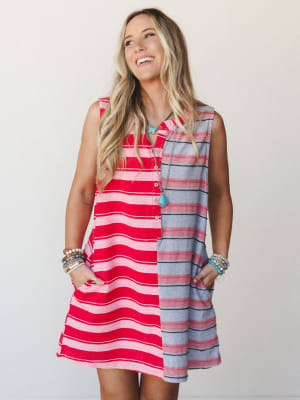 A color-blocked striped mini dress in bold red-pink and muted grey panels worn with stacked bracelets and a turquoise pendant necklace — easy, cheerful, and ready for wherever summer takes you.