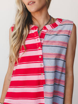 A close-up shot of a sleeveless color-block stripe dress in red and grey, styled with layered necklaces — the kind of effortless, lived-in piece that looks equally at home on a boardwalk or a back patio.