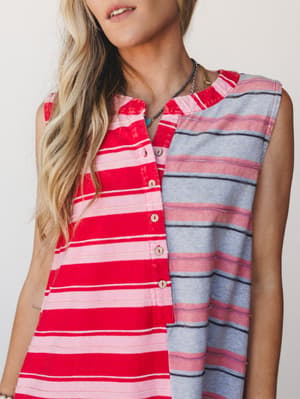 A close-up shot of a sleeveless color-block stripe dress in red and grey, styled with layered necklaces — the kind of effortless, lived-in piece that looks equally at home on a boardwalk or a back patio.