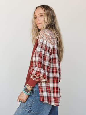 A relaxed, lived-in mixed-print top styled with stacked turquoise bracelets and denim — shot from a three-quarter back angle that shows off the patchwork flannel and floral yoke detail beautifully.