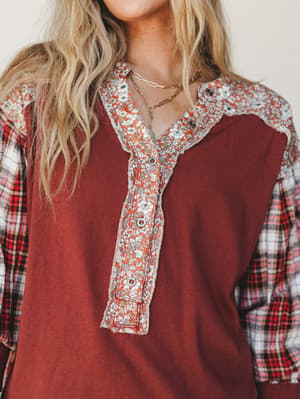 A close-up of a mixed-print top in deep burgundy with floral contrast panels at the neckline and shoulders, plaid sleeves, and snap button placket — the kind of top that looks like it was made from your three favorite shirts combined in the best poss