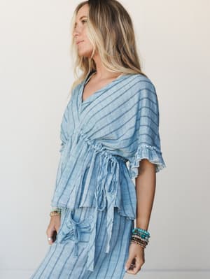 A breezy striped linen-look blouse in washed denim blue, styled with matching wide-leg pants and stacked turquoise and beaded bracelets — the kind of effortless set that looks like you packed it with intention.