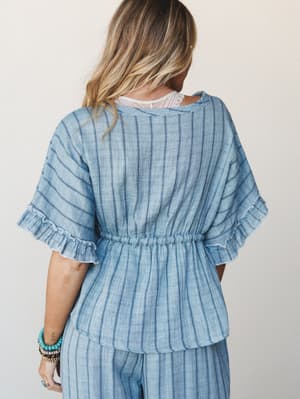 Shot from the back, a striped linen-look blouse with flutter sleeves and a cinched waist is styled with matching wide-leg pants — the lace peaking at the neckline and a stack of turquoise bracelets giving it that effortless, put-together-without-tryi