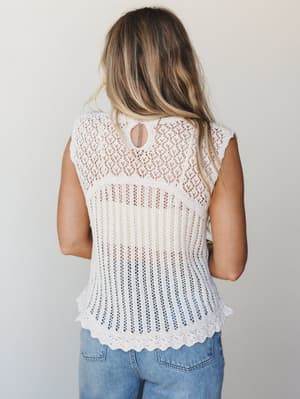 Shot from the back, this cream open-knit tank has a handmade, heirloom quality to it — the mix of diamond lace at the top and vertical open-knit ribbing below gives it real texture and softness, styled simply with light-wash jeans.