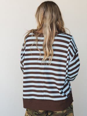 A back-view shot of a relaxed striped waffle-knit long sleeve top in mocha and sky blue, paired with camo pants — the kind of effortless, lived-in combo that looks like it happened on purpose.