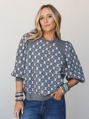 A relaxed, personality-packed top in charcoal with an all-over star/floral jacquard print and voluminous puff sleeves — styled with stacked beaded bracelets and denim for that effortless, expressive everyday look.