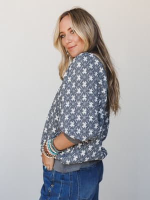 Shot from a three-quarter back angle, she glances over her shoulder with an easy smile — the star-print pullover feels like the kind of top you reach for without thinking, stacked bracelets and all.