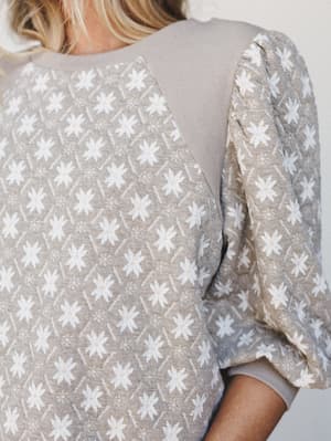 A close-up detail shot of a soft mushroom-toned top with an all-over daisy print and voluminous puff sleeves — the kind of top that feels like a cozy Saturday but looks like you tried.