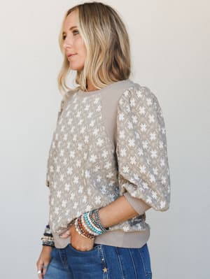 A relaxed printed top in warm mushroom and white gets styled with stacked beaded bracelets and dark denim — the kind of put-together-but-effortless combination that makes a Tuesday feel intentional.