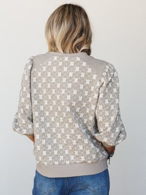 Shot from behind, a model in a taupe printed sweatshirt top with puff sleeves and contrast ribbed trim pairs it with denim — the kind of effortlessly cozy look that feels intentional without trying too hard.