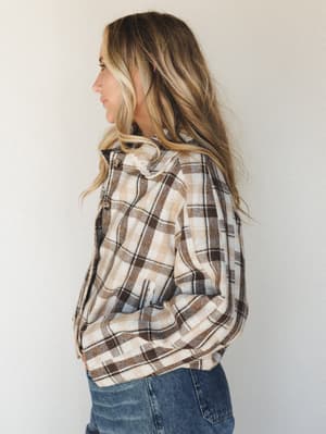A side-profile shot of a model in a warm plaid flannel top layered over jeans — the kind of top that makes a Saturday morning feel intentional.